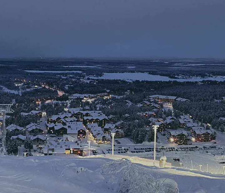 Levi village seen from the fell in blue winter light, chalets and lit streets below a snowy forest