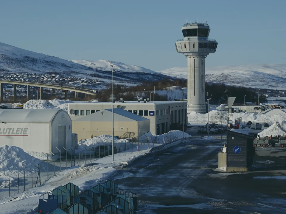 The control tower at Tromsø Airport above snow-covered hangars, with the Tromsø bridge and a snowy ridge behind