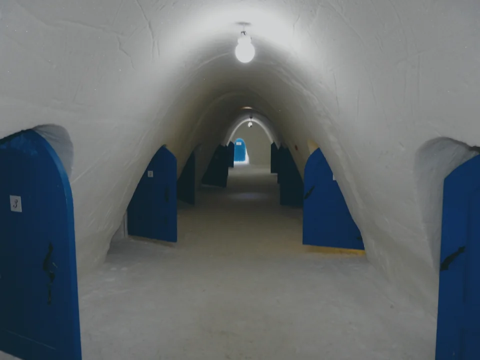 A snow-carved corridor lined with numbered blue room doors inside an ice hotel