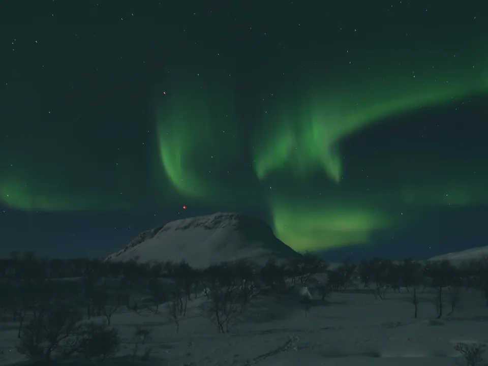 Green aurora bands swirling over the flat-topped Saana fell above a snow-covered valley at night