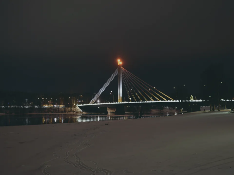The Jätkänkynttilä bridge in Rovaniemi lit on a December evening, snow on the bank and the river still open