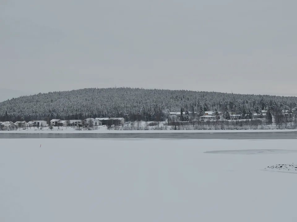 The wooded hill of Ounasvaara under snow across the frozen Kemijoki river, with the edge of Rovaniemi along its foot
