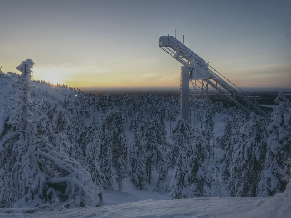 The ski jump tower at Ruka silhouetted against a dusk sky, with snow-laden trees in the foreground