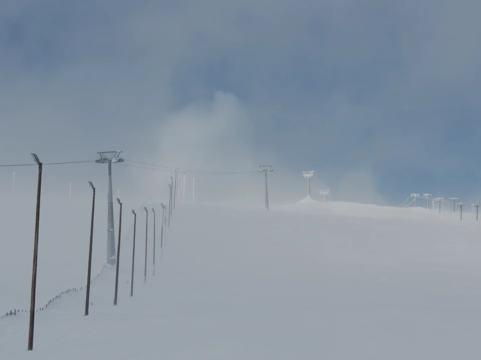 An empty ski lift line of poles and cable running up a wide, foggy slope into a deep blue sky, with nobody in view