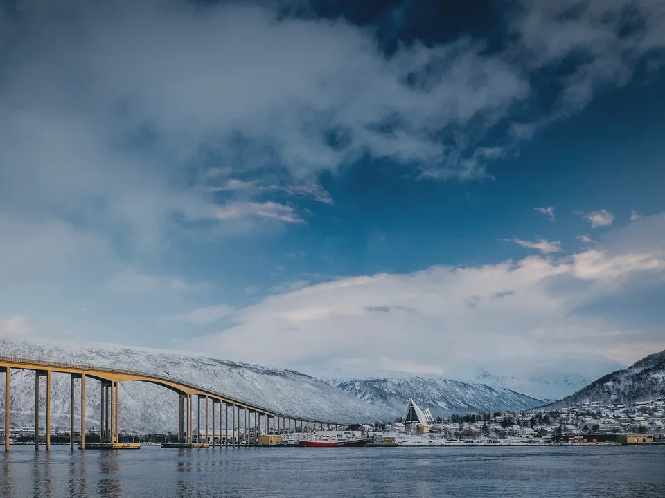 The Tromsø bridge curving across the strait in low winter light, the white triangular Arctic Cathedral on the far shore and snowy fells behind