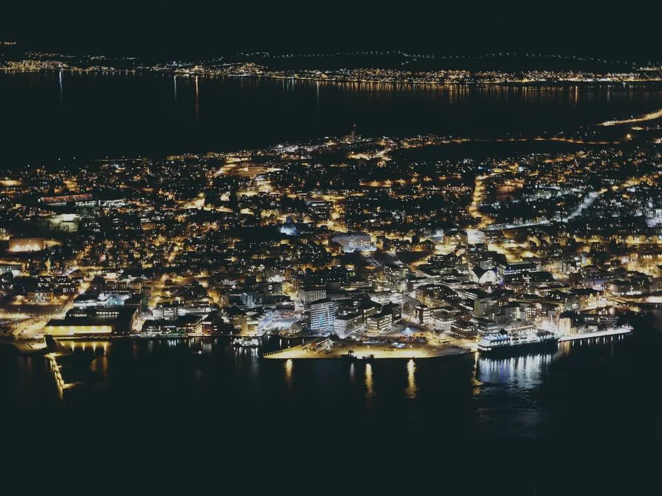 Tromsø at night from the fell above it, the lit street grid of the island filling the frame with the dark strait in front and behind